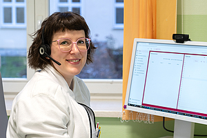 Eine lächelnde Frau mit einem Headset vor einem Computer.